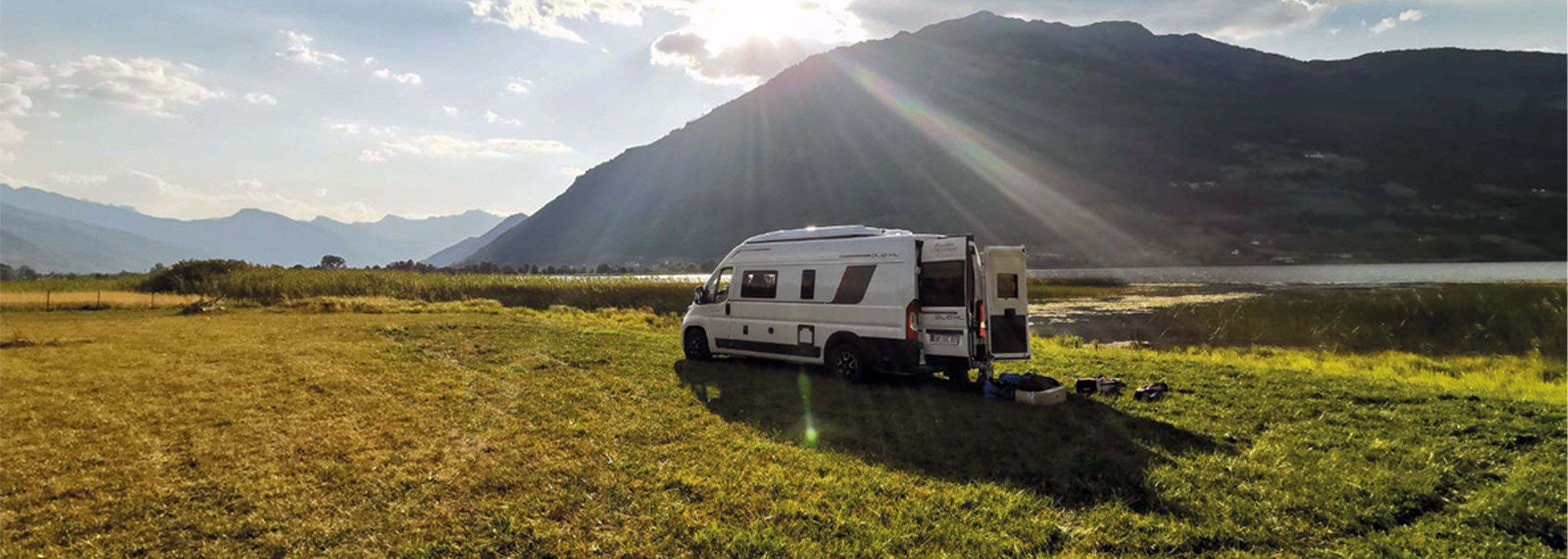 Ein Campervan stehend auf einer freien Wiese im Sonnenlicht vor einem Berg